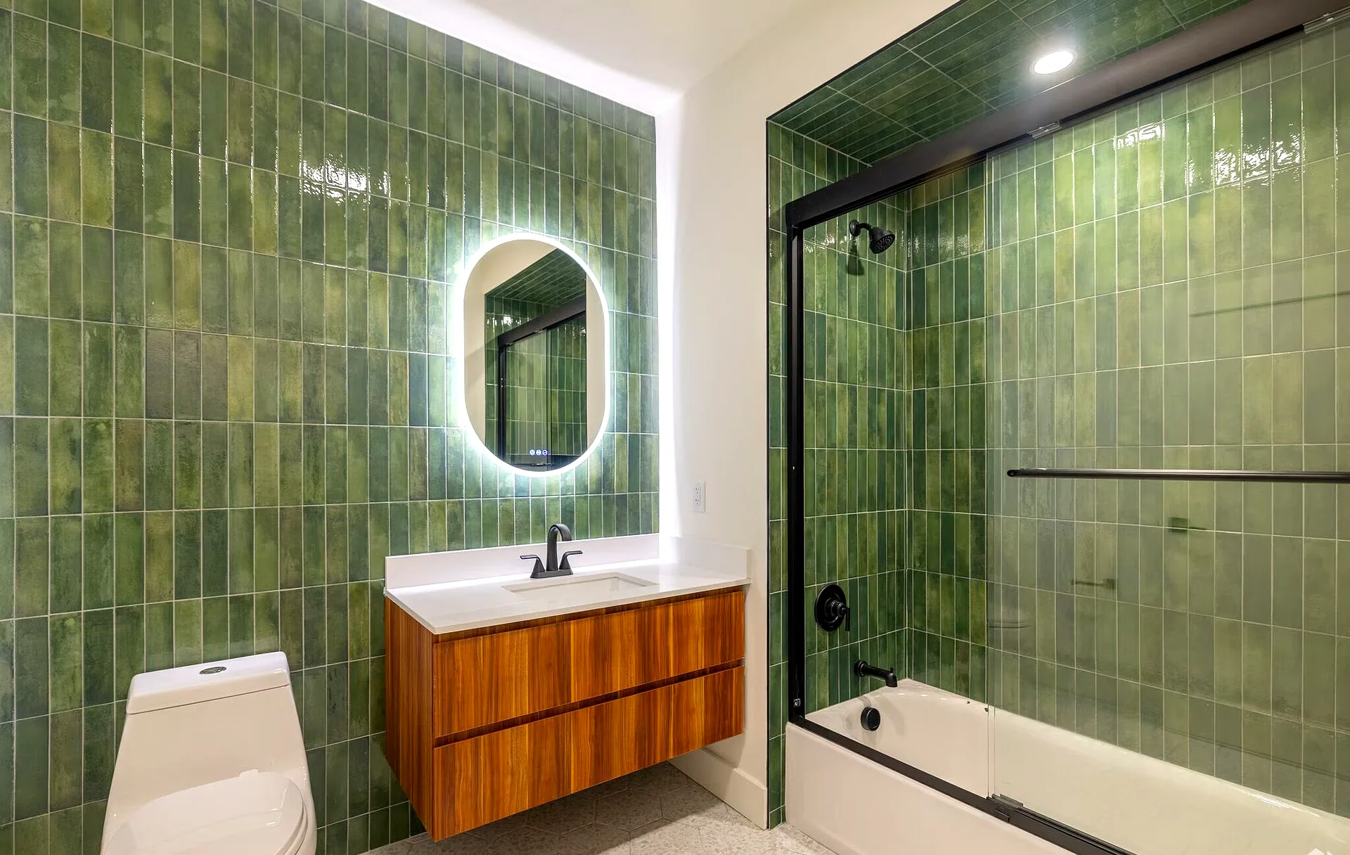 Full bath with green tile, a backlit round mirror, and a floating vanity