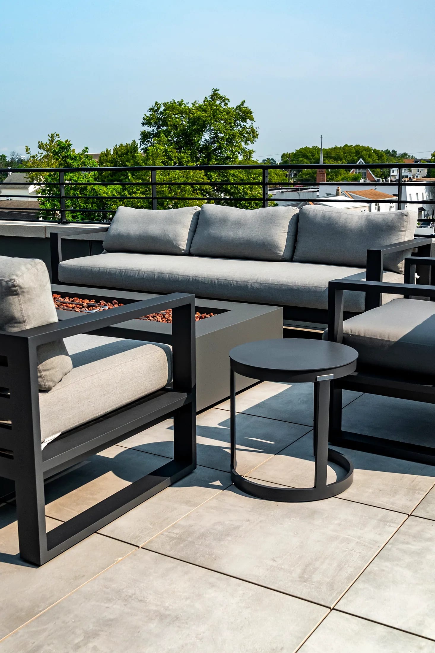 Sofá y mesa con fogata en la terraza con árboles más allá del barandal